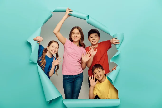 KONTAKT 4 Kinder schauen aus einer türkisen Papierwand heraus