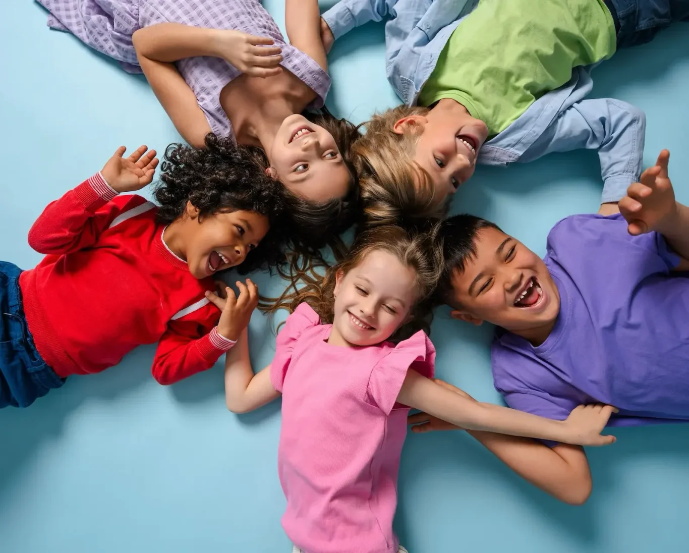 Wann wurde denn die Kinderherzpraxis in Linz gegründet? Sechs fröhliche Kinder liegen im Kreis auf einem blauen Boden und lächeln.