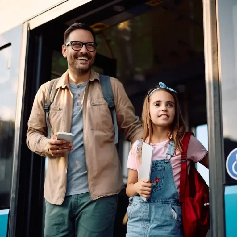 Anreise mit dem öffentlichen Verkehr in Linz Vater und Tochter steigen lächelnd aus einem Bus aus. Beide halten persönliche Sachen.