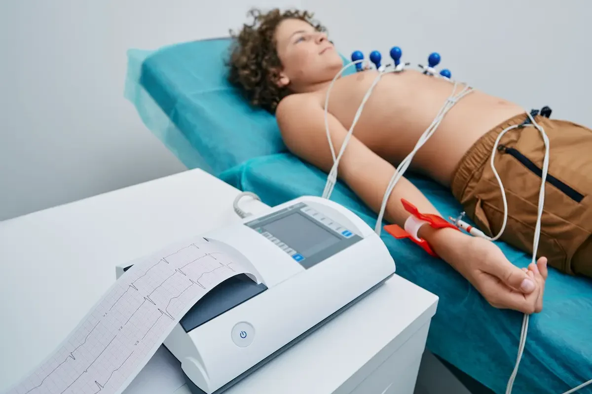 12-Kanal-EKG Untersuchung Ein junger Patient liegt auf einer Liege, verbunden mit einem EKG-Gerät, das gerade den Herzschlag aufzeichnet